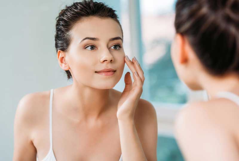 Young woman looking at face in mirror.